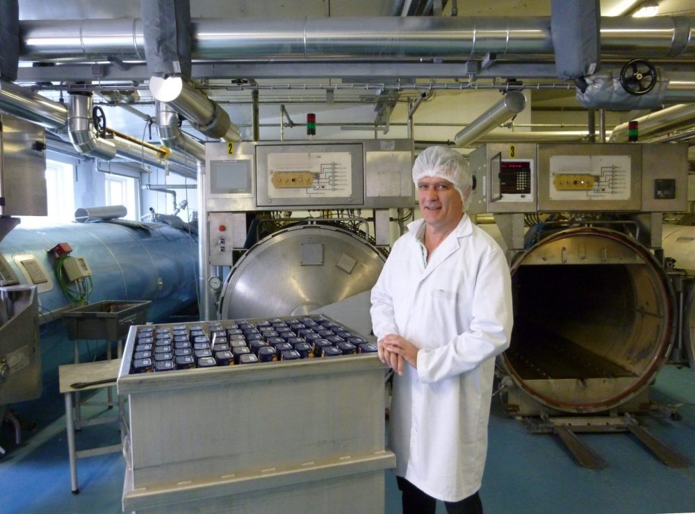 Photo de Alain Fournial devant un panier de stérilisation rempli dans un atelier de production industrielle comprenant plusieurs autoclave statiques.